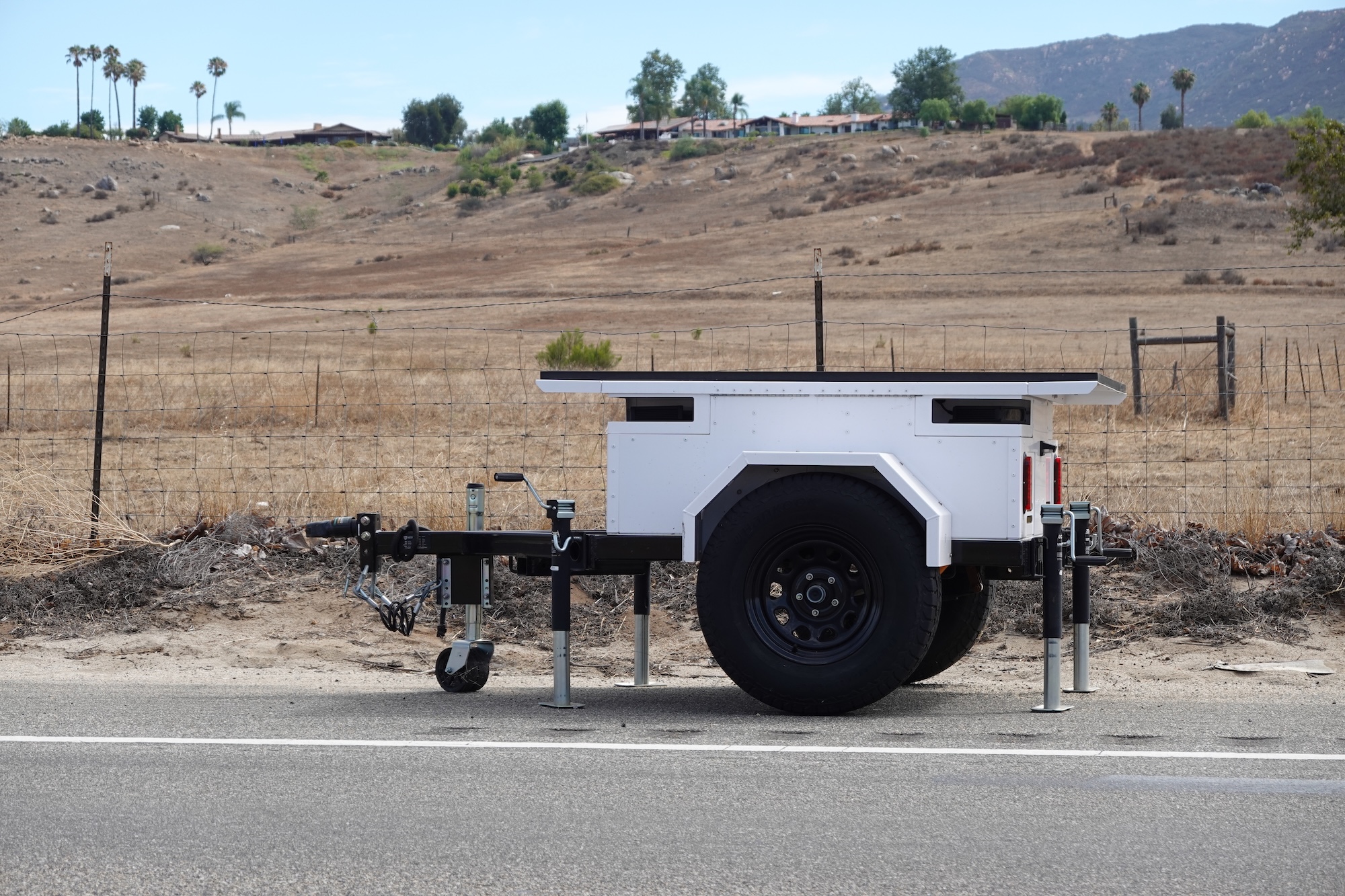 A white flat trailer by the side of the road with camera portals on either end. A white flat trailer by the side of the road with camera portals on either end.
